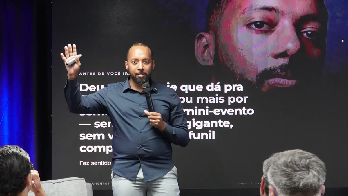 Mateus Menezes no palco durante um evento presencial da Reino, com a plateia em mesas
